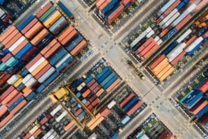 Aerial view of a busy shipping container terminal with colorful cargo containers organized in rows and transportation lanes.