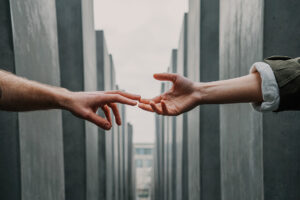 Two hands almost touching across a narrow concrete corridor, symbolizing connection, distance, and the bridging of human gaps.