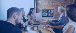 Business team in a conference room attending a hybrid meeting with remote participants on a screen via video conferencing software.