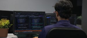 Software developer working at a dual-monitor setup writing and debugging code in a modern office environment with Visual Studio