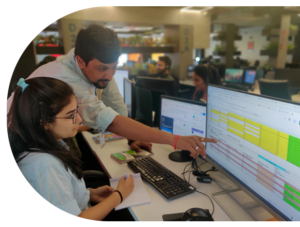 A software developer and quality analyst collaborate on a computer in a Top IT Company in India, focused on their work.